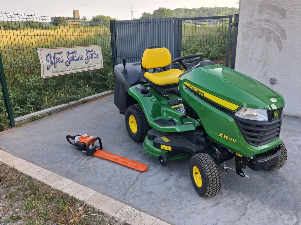 Tracteur tondeuse John Deere X350R et taille-haie devant la bâche Meca Soudure Service