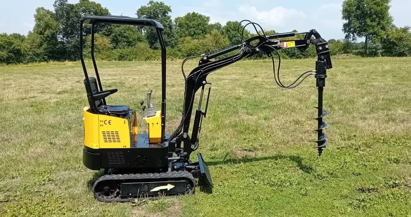 La mini-pelle de location équipée de la tarière, dans un pré